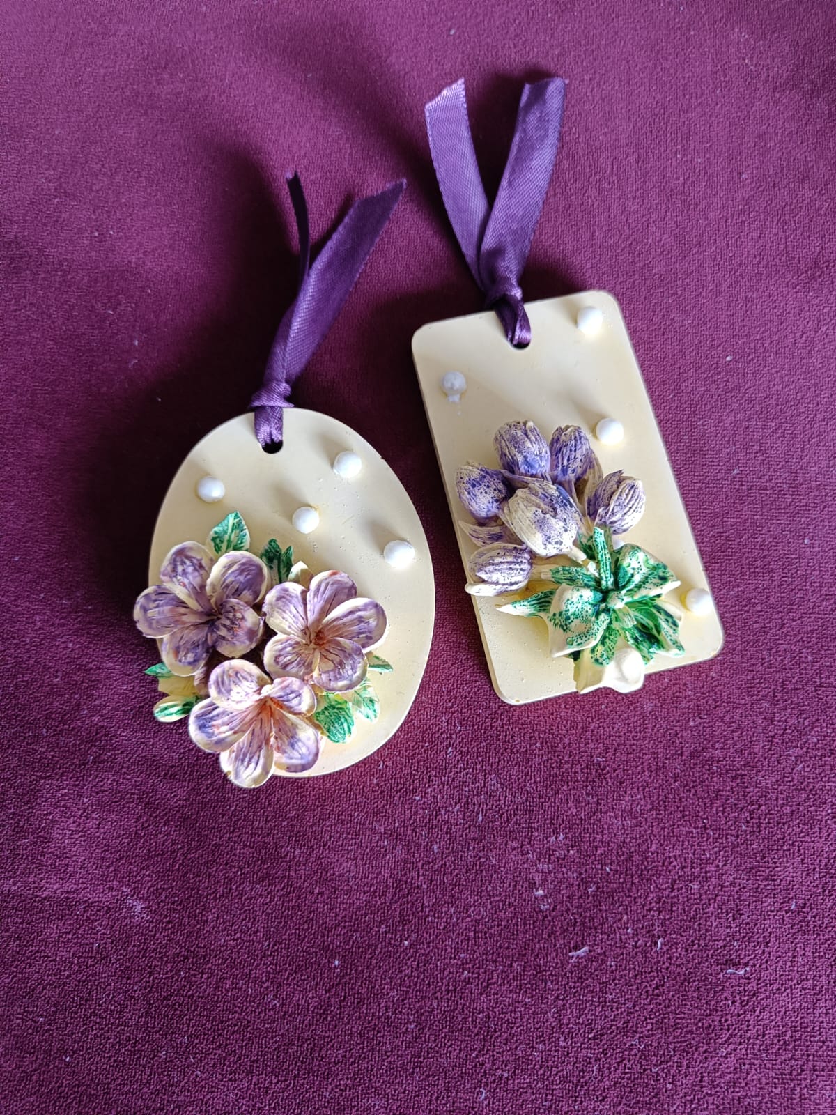 Two hanging aroma stone tags with purple floral designs and ribbons