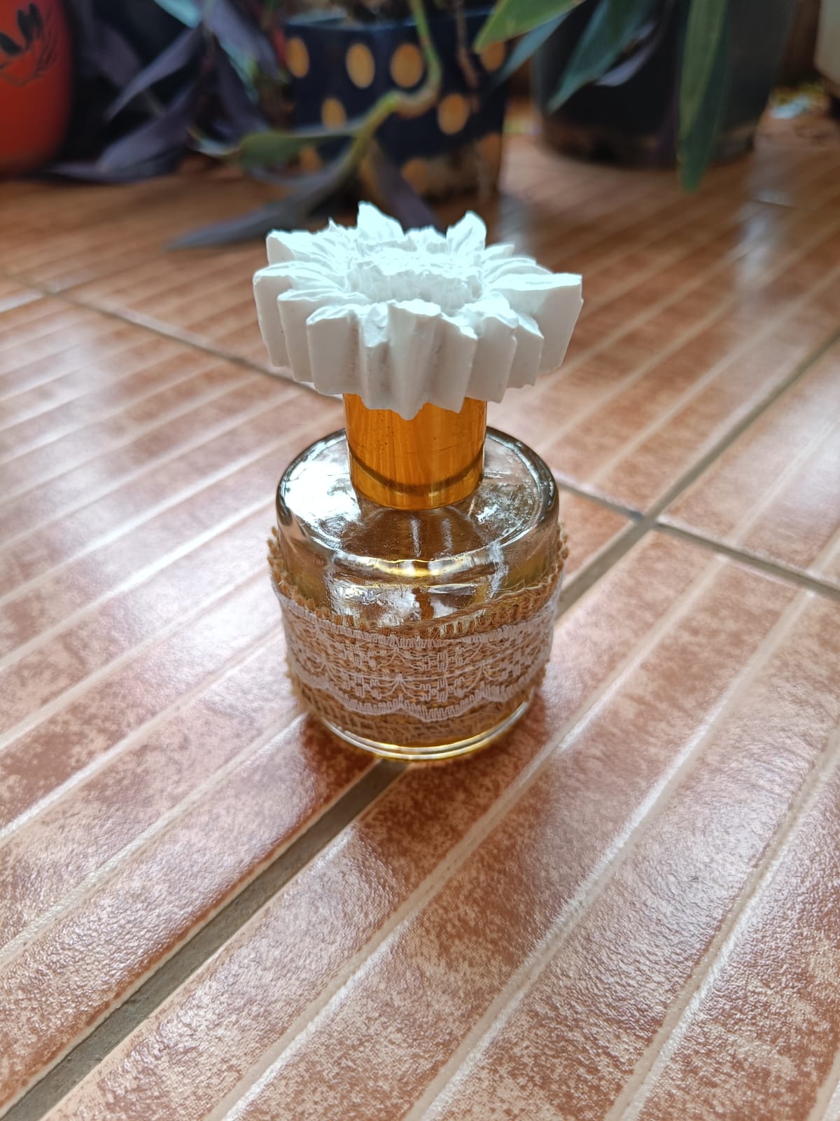 White flower diffuser stopper on a lace-wrapped glass bottle